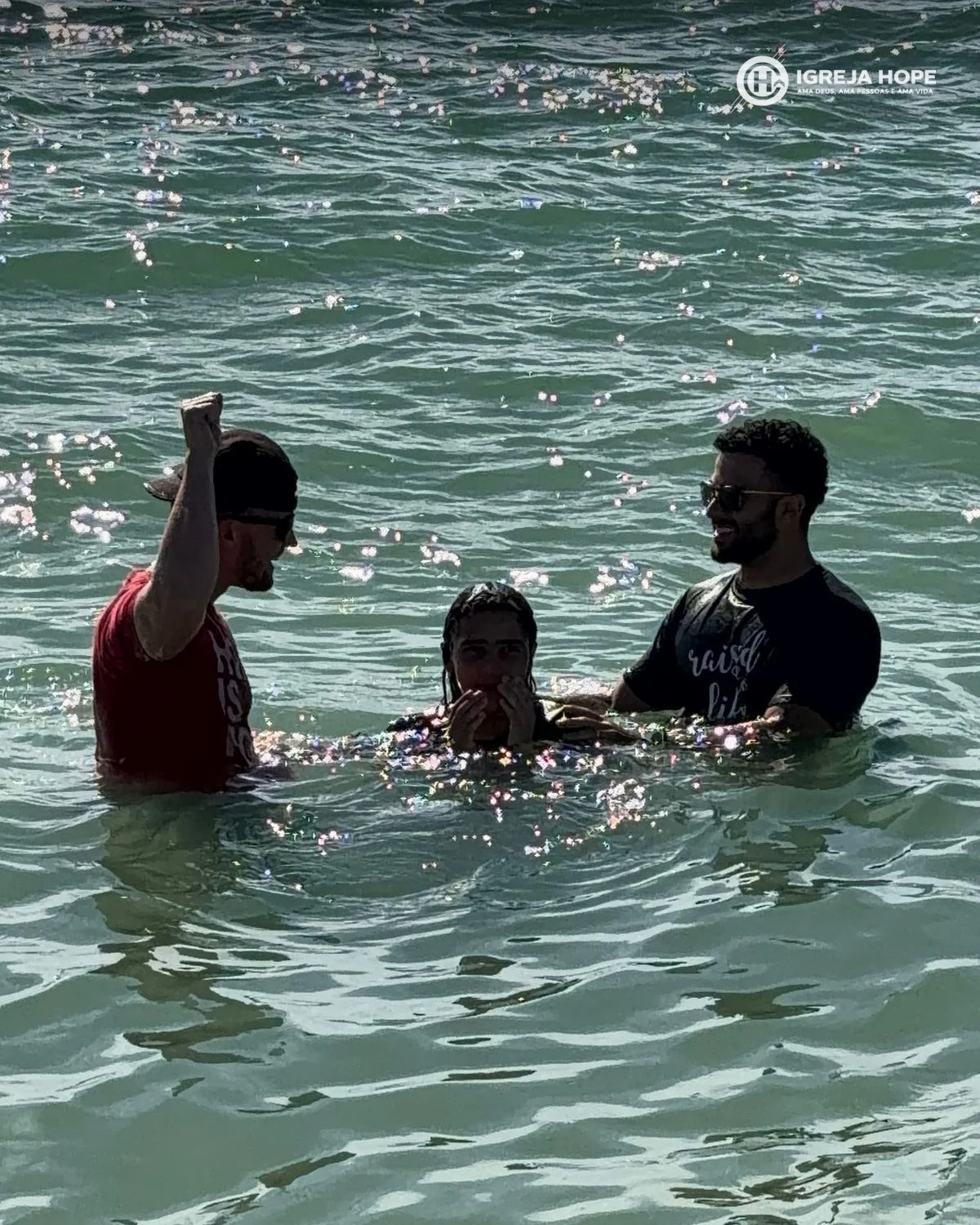 Momento do batismo no mar em Turtle Beach — uma jovem sendo imersa entre dois pastores da Igreja Hope Sarasota